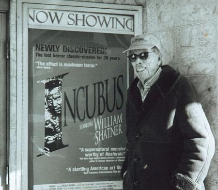 Anthony M. Taylor, producer of Incubus (1966), poses in front of a poster for the film